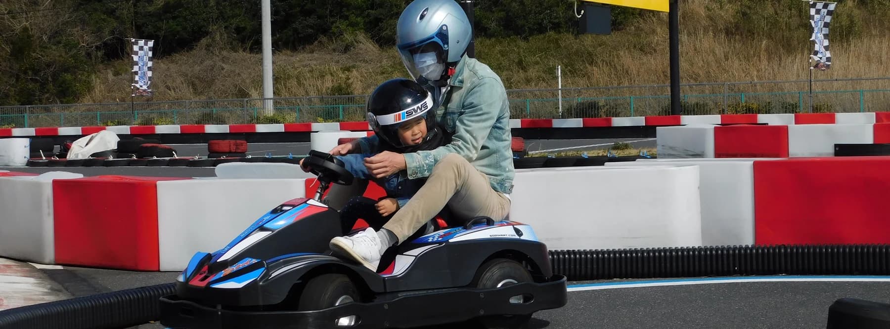 A young child in a helmet standing beside kids karts